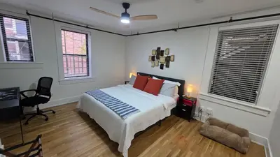 a bedroom with a bed and a chair and two windows at Quiet cheerful condo in the heart of OTR! in Cincinnati