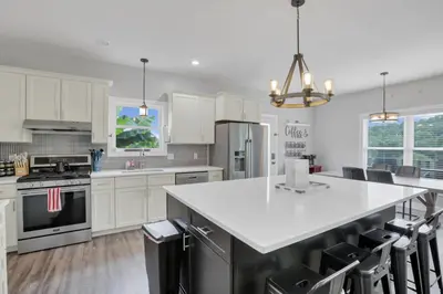 a kitchen with white cabinets and a large island with chairs at Serenity on Siverly by Purple Munky Hospitality in McArthur