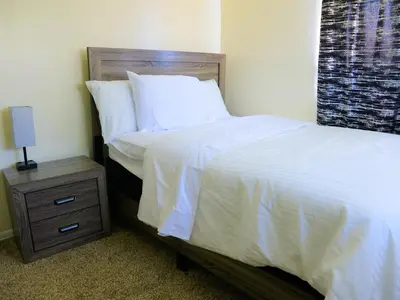 a bed with white sheets and a night stand with a lamp at A Nice and Cozy Home in Fairborn in Fairborn