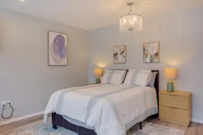 a white bedroom with a bed and a chandelier at Cozy 12th-Floor Studio with Lake Erie Views! in Lakewood