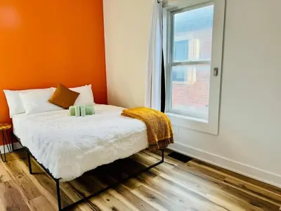 a bedroom with a bed with an orange wall and a window at Cozy Casita by Jungle House Downtown & Short North Free Parking 5 800 Reviews Near Convention Center & Nationwide Arena & Ohio State Walk to High Street in Columbus