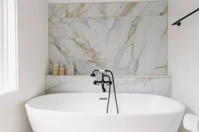 a white bath tub in a bathroom with marble walls at “Ivory Inn” - Cozy Modern Stay w/ Hot Tub - LEX in Lexington