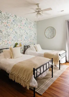 two beds in a room with floral wallpaper at 