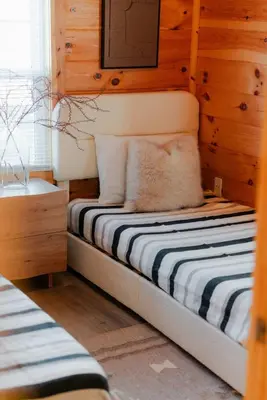a small bed in a room with wooden walls at Cedar Wrapped Cozy Villa Cabin - 4 miles from Trails in Laurelville