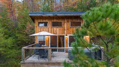 a cabin in the woods with a deck and an umbrella at The Dragonfly - Tiny Mountaintop Cabin with Hot tub in Stanton