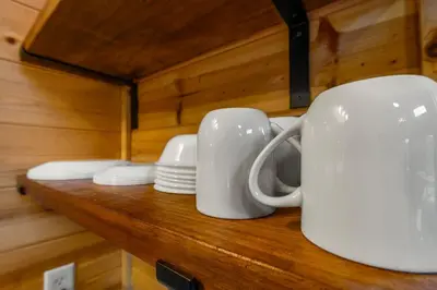 three white cups and plates on a wooden shelf at The Dragonfly - Tiny Mountaintop Cabin with Hot tub in Stanton