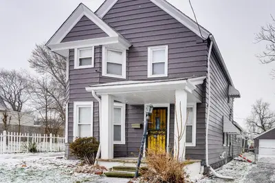 a gray house with a yellow door and a fence at 8 Mi to Dtwn CLE Cozy Couples Retreat with Gym! in Cleveland