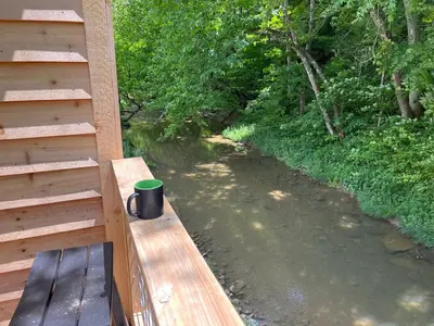 a cup sitting on a wooden bench next to a river at The Owl's Perch Treehouse