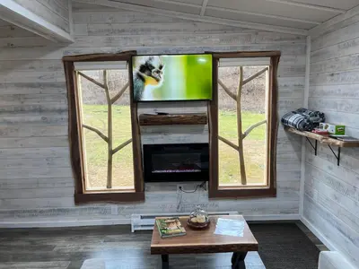 a living room with a tv and two windows at The Owl's Perch Treehouse