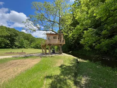 a tree house in a field next to a river at The Owl's Perch Treehouse
