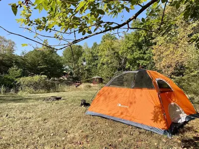 an orange tent sitting in a field under a tree at Breath of Heaven Cabin- Hot Tub, Deck, Pond, PETS in Logan