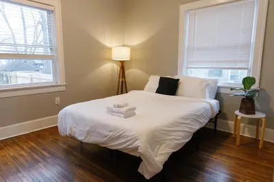 a bedroom with a bed with white sheets and a lamp at The Avon - Quaint Home in Downtown Lexington in Lexington
