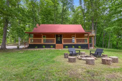 a log cabin in the woods with chairs and a fire pit at Furnace Mountain Retreat- Hot Tub, Fireplace, WiFi in Stanton