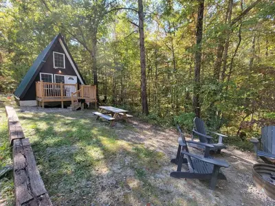a cabin in the woods with a picnic table and benches at A Frame of Mind - near Red River Gorge KY in Jeffersonville