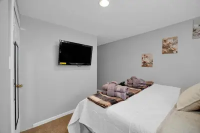 a white bedroom with a bed with a tv on the wall at The Little Paradise in Morrow