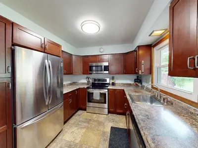 a kitchen with wooden cabinets and a stainless steel refrigerator at Rustic Kirtland Farmhouse Retreat in Kirtland