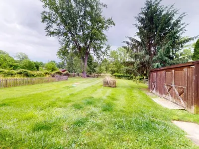 a grassy yard with a fence and trees at Rustic Kirtland Farmhouse Retreat in Kirtland