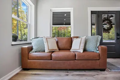 a brown couch in a living room with windows at Pine Grove Barndominium in Sugar Grove