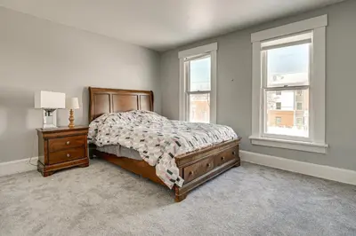a bedroom with a bed and a nightstand and two windows at Walk to Trolley District Olde Towne East Retreat in Columbus