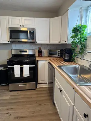 a kitchen with white cabinets and a stove and a sink at The Cozy Cottonwood Cottage- Clintonville 3BRM Ranch in Columbus
