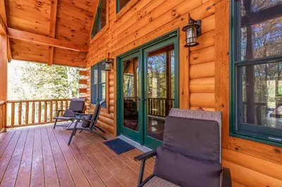 a porch of a wooden cabin with chairs and windows at Whiskey Ridge in Logan