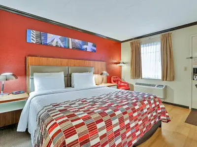 a hotel room with a bed and a red wall at Red Roof Inn Uhrichsville in Uhrichsville