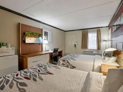 a hotel room with two beds and a desk at Red Roof Inn Uhrichsville in Uhrichsville
