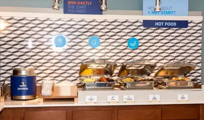a counter with several trays of food on it at Holiday Inn Express Hotel & Suites Madison by IHG in Madison
