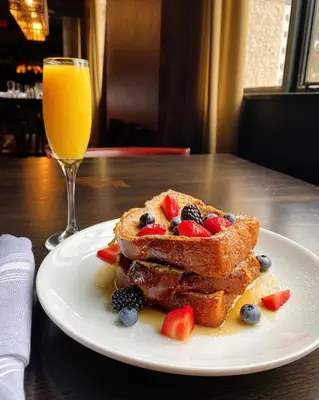 a plate of french toast with fruit and a glass of orange juice at Hotel LeVeque, Autograph Collection in Columbus