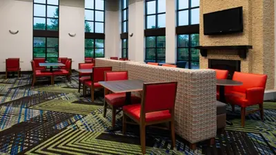 a waiting room with red chairs and tables and a fireplace at Holiday Inn Express Cincinnati West by IHG in Dent