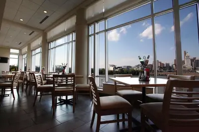 a restaurant with tables and chairs and large windows at Embassy Suites Cincinnati - RiverCenter in Covington