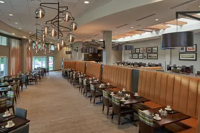 a dining room with tables and chairs and a bar at Hilton Cincinnati Airport in Florence