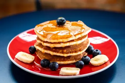 a stack of pancakes with blueberries and bananas on a red plate at Crowne Plaza Cleveland Airport by IHG in Middleburg Heights