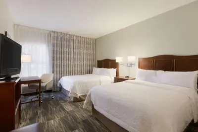 a hotel room with two beds and a flat screen tv at Hampton Inn Zanesville in Zanesville