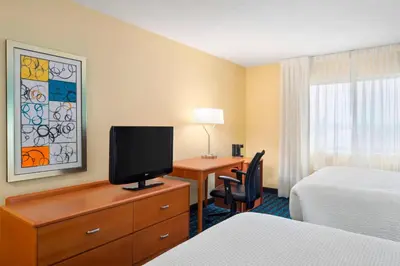 a hotel room with a desk with a tv and a bedroom at Fairfield Inn & Suites Lima in Lima