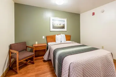 a small bedroom with a bed and a chair at HomeTowne Studios by Red Roof Columbus in Columbus