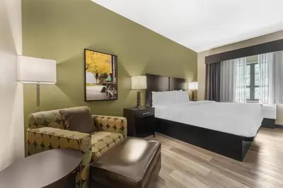a hotel room with a bed and a chair at Best Western Plus Franciscan Square Inn & Suites Steubenville in Steubenville
