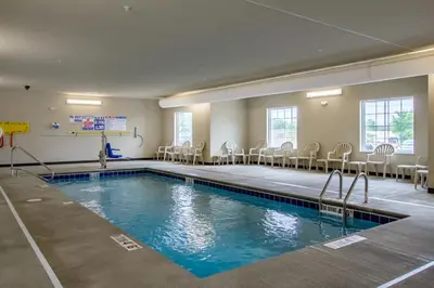 a swimming pool in a room with chairs and tables at Cobblestone Hotel & Suites - Orrville in Orrville