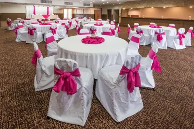 a room with white tables and chairs with pink bows at Columbus Grand Hotel & Banquet Center in Columbus