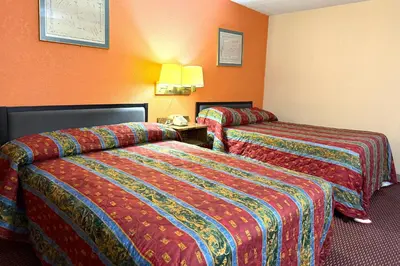 two beds in a hotel room with orange walls at Red Carpet Inn & Suites Lima -Listing Partner in Lima