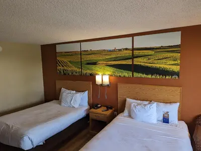 two beds in a hotel room with a painting on the wall at Days Inn by Wyndham Columbus Fairgrounds in Columbus