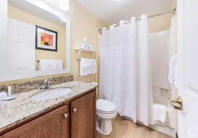 a bathroom with a white shower curtain and a toilet at Birch Hills Suites - Blue Ash in Blue Ash