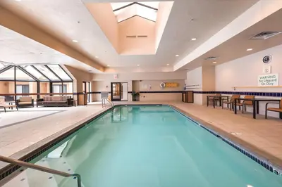 a swimming pool in a hotel lobby with a table and chairs at Courtyard Toledo Airport Holland in Holland