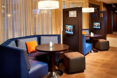 a waiting room with blue chairs and tables and televisions at Courtyard Toledo Airport Holland in Holland