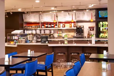 a restaurant with tables and blue chairs and a bar at Courtyard Toledo Maumee/Arrowhead in Maumee