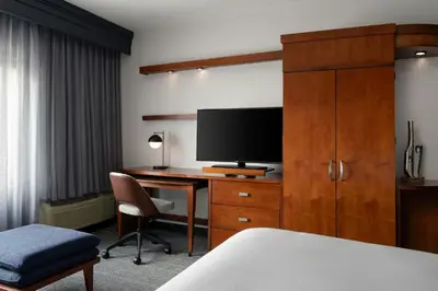 a hotel room with a desk with a tv and a bedroom at Courtyard Dayton-University of Dayton in Dayton