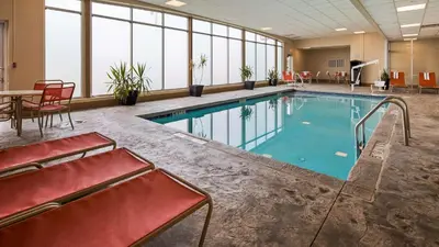 a large swimming pool with red chairs and a table at Best Western Airport Inn & Suites Cleveland in Brook Park