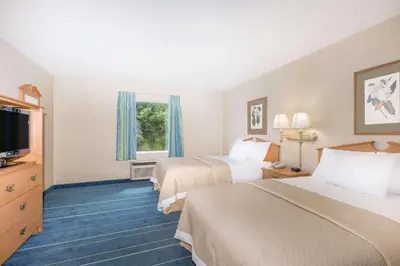 a hotel room with two beds and a flat screen tv at Days Inn & Suites by Wyndham Bridgeport - Clarksburg in Bridgeport