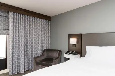 a bedroom with a bed and a chair next to a window at Hampton Inn Cincinnati Airport South in Florence