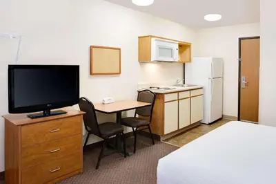 a hotel room with a desk with a television and a kitchen at WoodSpring Suites Fort Wayne in Fort Wayne